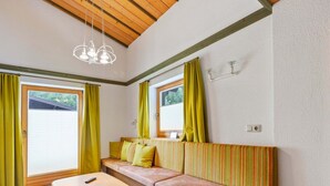 Ein Zimmer mit Holzboden, einer Bank mit gestreiften Kissen, einem Holztisch und einem Fenster mit Vorhängen.