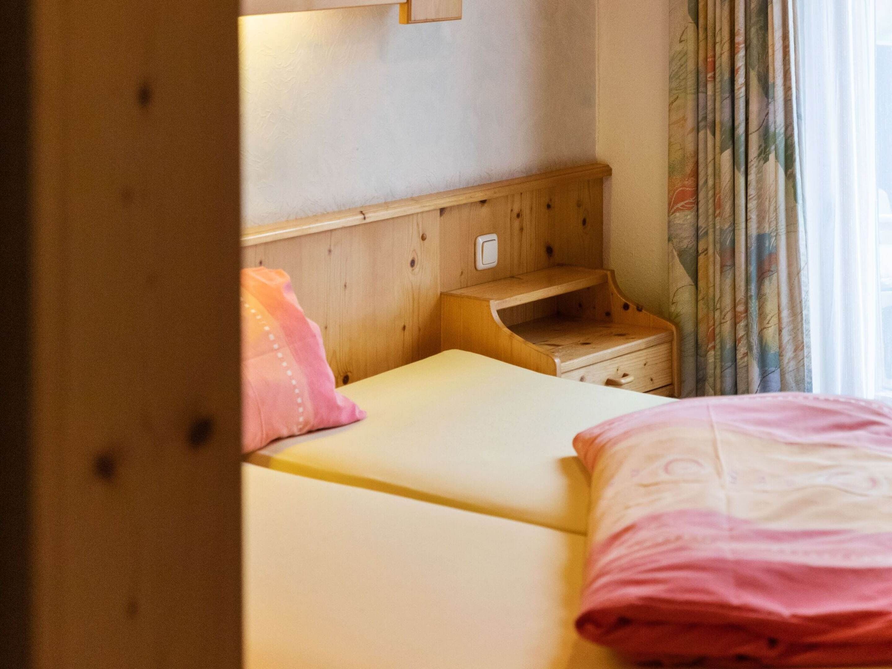 A bedroom with two beds, wooden headboard, bedside tables, and a window with curtains.