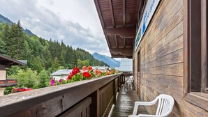 Ein Holzbalkon mit einem weißen Plastikstuhl, der einen Blick auf eine Berglandschaft mit roten Blumen und einen Blick auf ein Gebirge bietet.