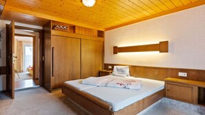 Ein Schlafzimmer mit Holzboden, einem Bett mit weißer Bettwäsche, einem Nachttisch und einem Kleiderschrank.