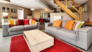 A modern living room with two grey sofas, a wooden coffee table, and a red rug. A staircase with wooden railings is visible in the background. - Stylish Holiday Home in Houffalize With Sauna, Patio, Garden (Houffalize)