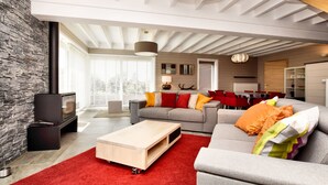 A modern living room with a stone accent wall, a grey sofa with colorful cushions, a wooden coffee table, and a red rug. - Stylish Holiday Home in Houffalize With Sauna, Patio, Garden (Houffalize)
