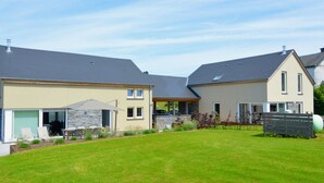 A modern residential house with a well-maintained lawn, a patio area, and a stone facade. - Stylish Holiday Home in Houffalize With Sauna, Patio, Garden (Houffalize)