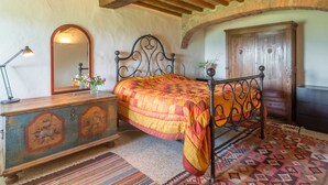 Ein Schlafzimmer mit einem hölzernen Bett, einem Schminktisch mit floraler Dekoration, einem Spiegel und einem gemusterten Teppich.