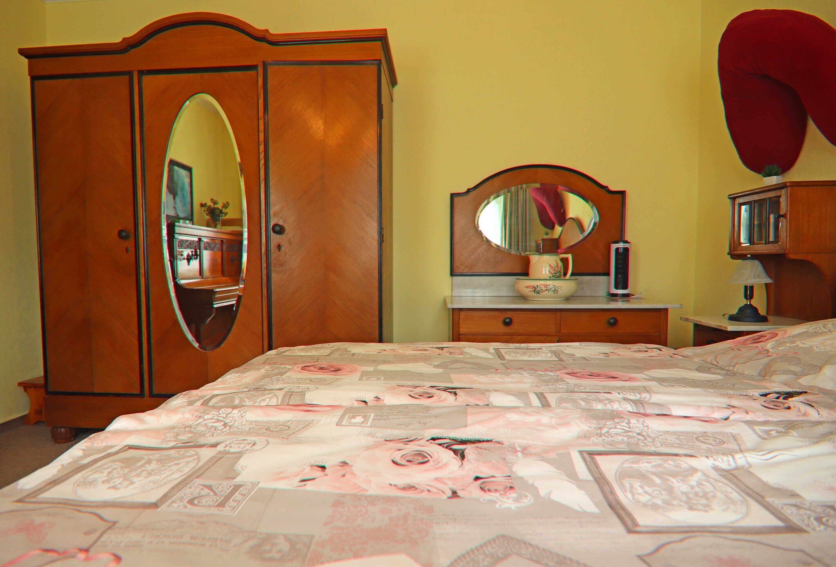 A bedroom with a large bed, a wooden wardrobe, a dresser, and a mirror.