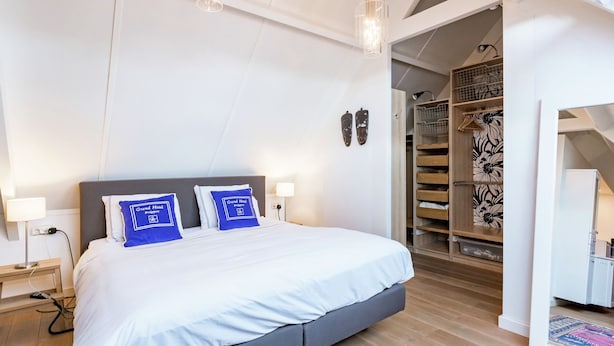 A modern hotel room with a large bed, a wooden floor, a wardrobe, and a small desk with a lamp. - Cottage in Ovezande With Terrace (Ovezande)