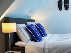 A neatly made bed with white bedding and blue pillows, a bedside lamp, and a wall-mounted shoe rack. - Cottage in Ovezande With Terrace (Ovezande)