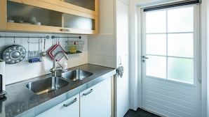 A kitchen with a stainless steel sink, wooden cabinets, a window, and a door. - Cottage in Ovezande With Terrace (Ovezande)
