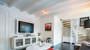 A modern living room with a flat-screen TV, white cabinetry, a white coffee table, and a patterned rug. - Cottage in Ovezande With Terrace (Ovezande)