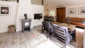 A modern living room with a stone floor, a fireplace, a dining area, and a sofa. - Beautiful Holiday Home With Sauna (Heino)