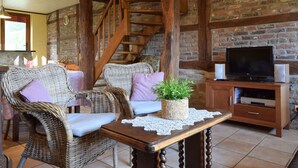 A cozy living room with wicker furniture, a wooden staircase, and a television. - Cozy Family Stay in Durbuy (Durbuy)