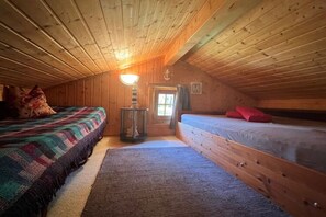A cozy attic bedroom with wooden walls and a sloped ceiling. There are two beds with colorful bedding and a small table with a lamp. - Log Cabin Near Baltic Sea Lighthouse (Bastorf)