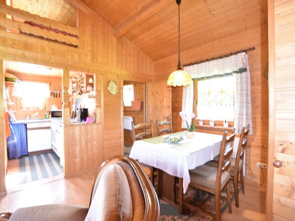 A wooden cabin interior with a dining area, kitchen, and a clock on the wall. - Log Cabin Near Baltic Sea Lighthouse (Bastorf)