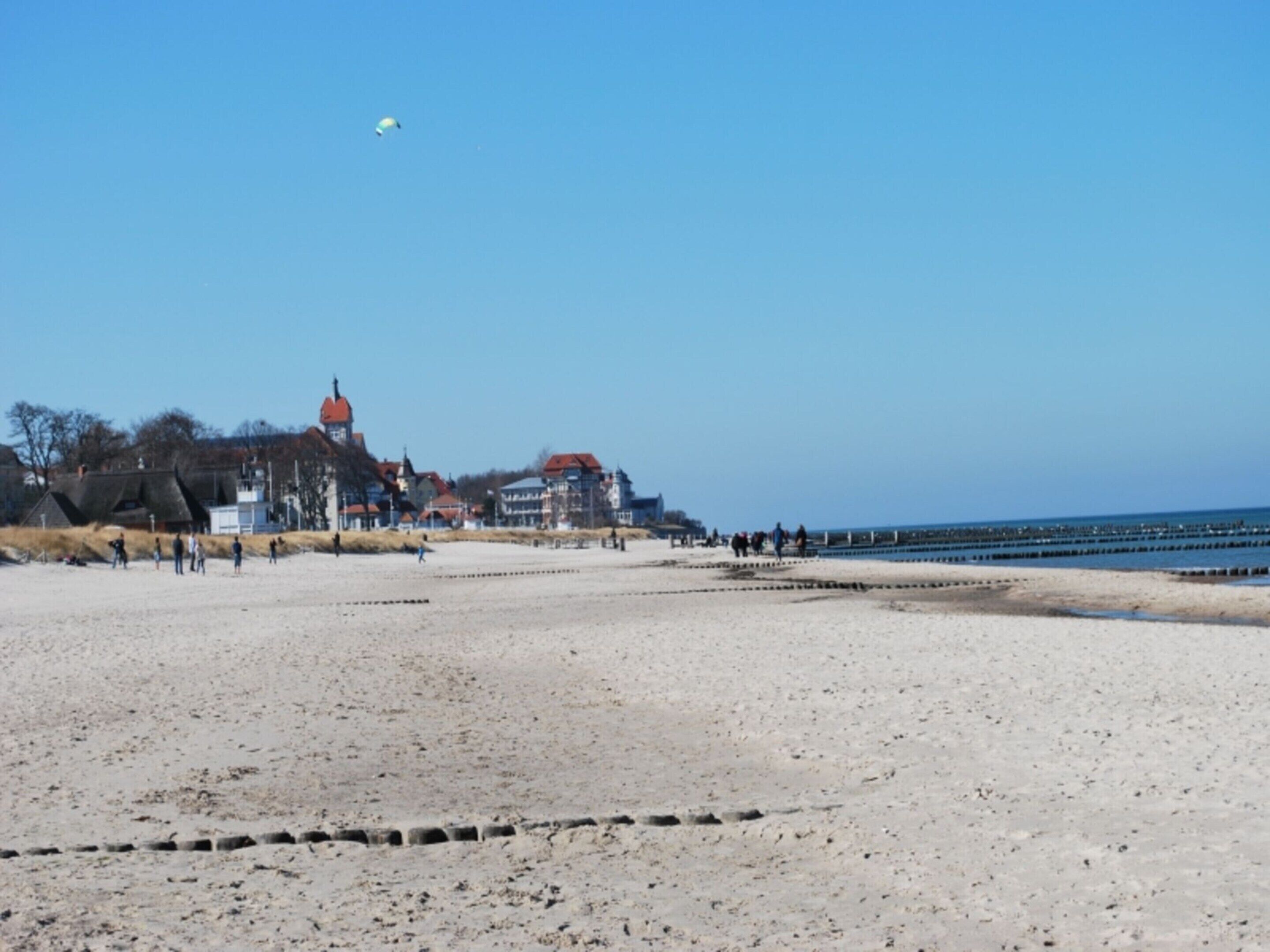 A beach with a clear sky, a few people, and buildings in the background.