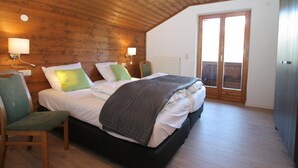 Een slaapkamer met een houten plafond, een bed met witte beddengoed en groene kussens, een stoel en een schuifdeur naar een buitenruimte.