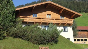 Een houten chalet met een schuin dak, een bord met de tekst 'P. Kristall', en een bergachtige achtergrond.