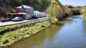 A riverside property with a stone building, a red section, and a white building with a covered porch.