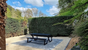 A picnic table in a garden area with a hedge and gravel path.