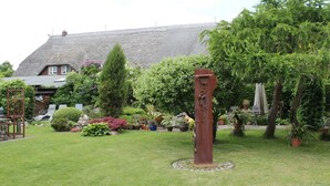 A garden with a sculpture, a thatched-roof house, and various plants. - Ferienwohnung Gerda in Ostseenahe (Wittenbeck)