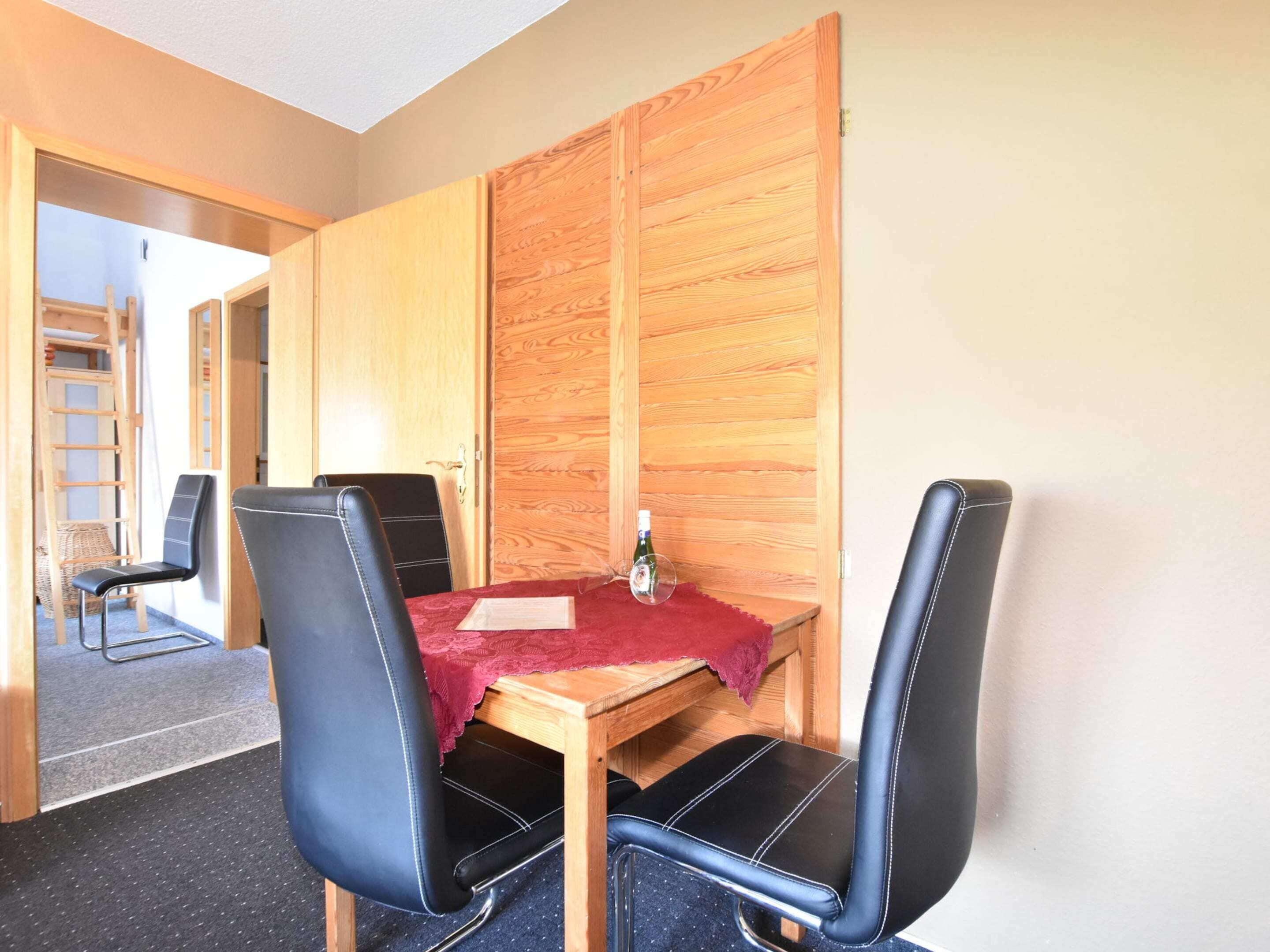 Ein Zimmer mit einem Holztisch, vier schwarzen Stühlen, einem Holzschrank und einer Leiter im Hintergrund.