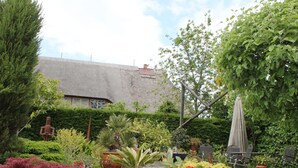 A garden with various potted plants, a statue, and a thatched-roof building. - Ferienwohnung Gerda in Ostseenahe (Wittenbeck)