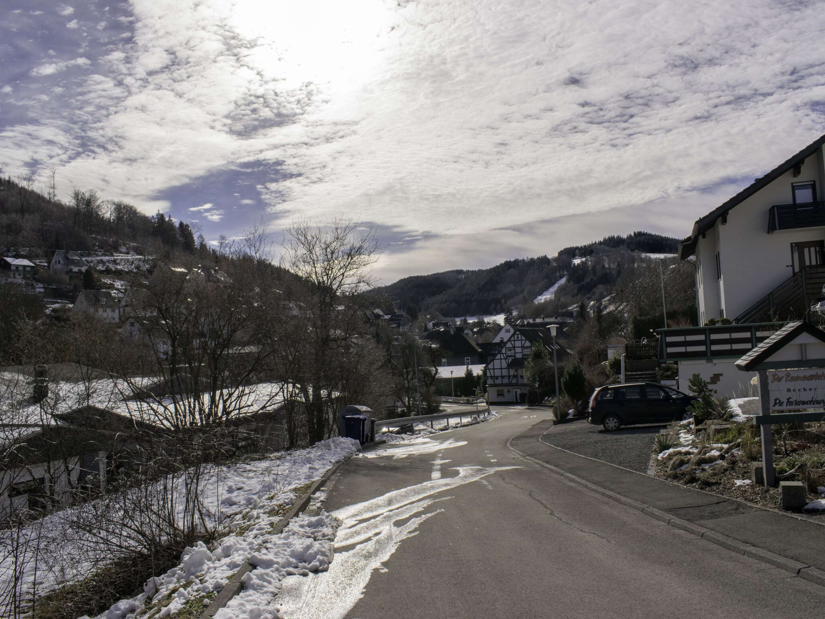 A snow-covered street in a small town with houses and a car parked on the side.