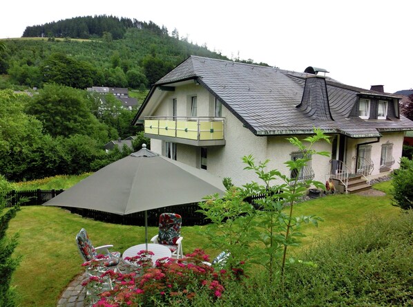 A two-story house with a sloped roof, a balcony, and a garden with a table and chairs. - Ferienwohnung in der Nahe des Skigebietes (Willingen)