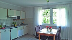 A compact kitchen with white cabinets, a microwave, and a dining table with chairs. - Ferienwohnung in der Nahe des Skigebietes (Willingen)