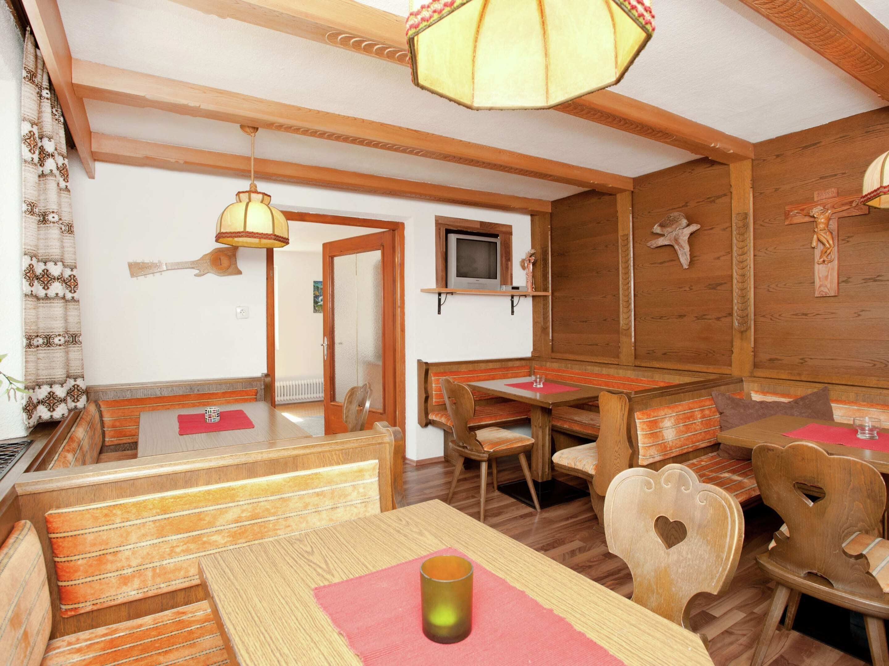 A cozy dining area with wooden benches and tables, a television mounted on the wall, and a ceiling fan.