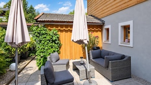 Une terrasse dotée de meubles en osier, de deux parasols et d’une clôture en bois.