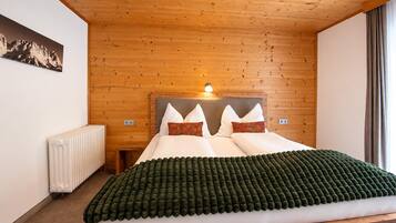 A bedroom with a wooden ceiling, a bed with white and orange pillows, a green blanket, and a radiator.