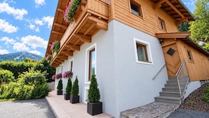 Un chalet en bois doté d’un balcon, de plantes en pot et d’un escalier en pierre.