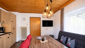 Une cuisine moderne avec des meubles en bois, une table à manger avec des chaises rouges, un canapé noir avec des coussins gris et une grande fenêtre avec des rideaux.