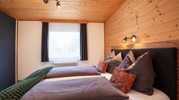 Ein Schlafzimmer mit Holzboden, einem Bett mit vielen Kissen, einem Fenster mit Vorhängen und einer Heizung.