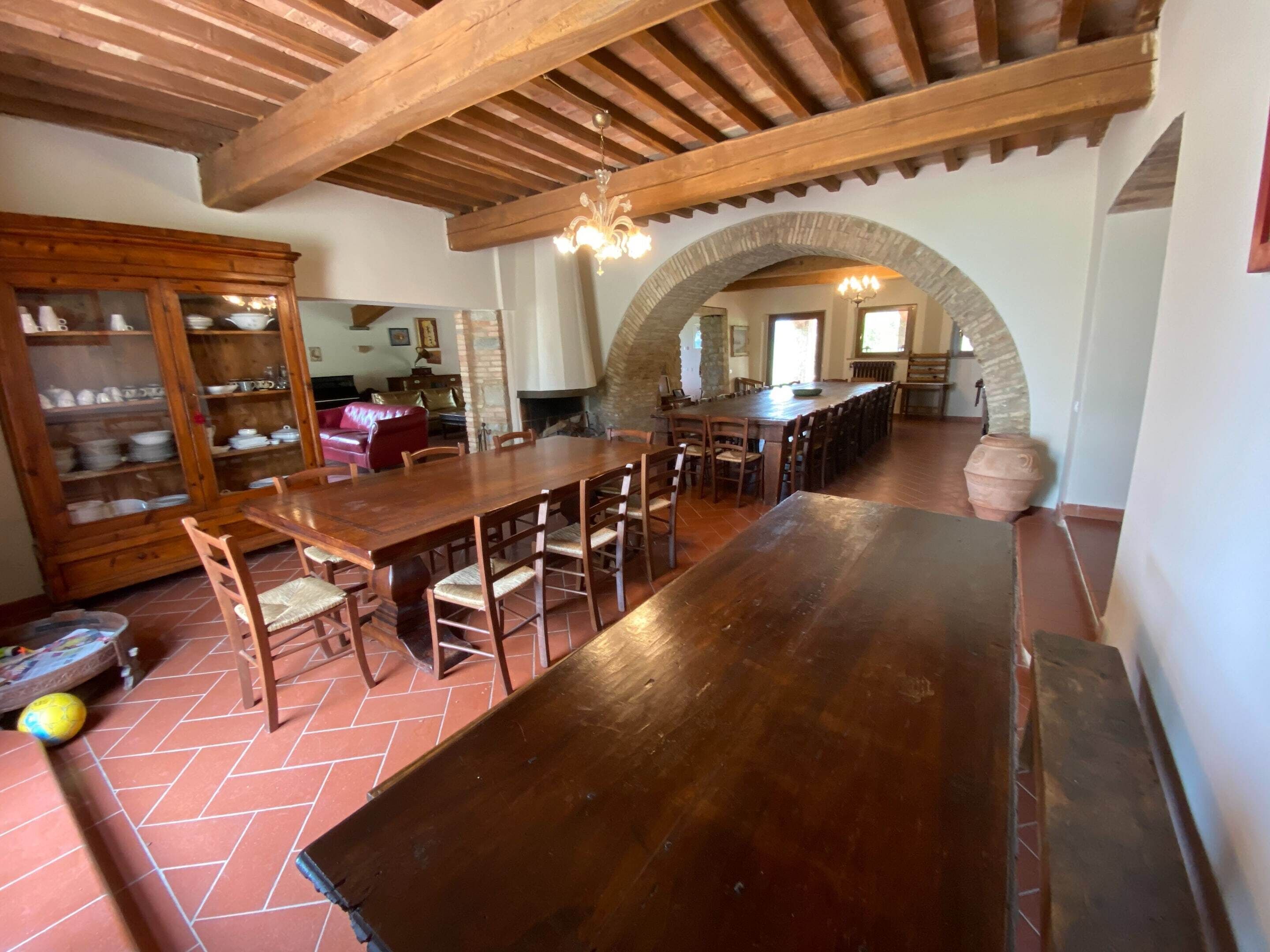A spacious dining area with a long wooden table and chairs, a built-in cabinet with glass doors, and a stone archway leading to another room.