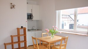 A small kitchen with a dining table and chairs, a microwave, and a window with a view of buildings outside. - Wohnung mit Eigener Terrasse in Huddingen (Bad Wildungen)