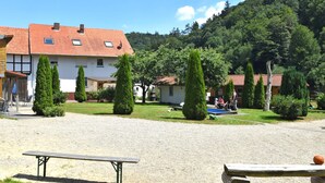 A courtyard with a gravel ground, a wooden bench, and a building with a red-tiled roof. - Wohnung mit Eigener Terrasse in Huddingen (Bad Wildungen)