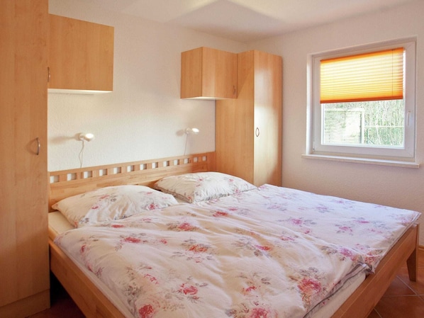 A bedroom with a wooden bed frame, two bedside tables with lamps, a window with blinds, and a wooden wardrobe.