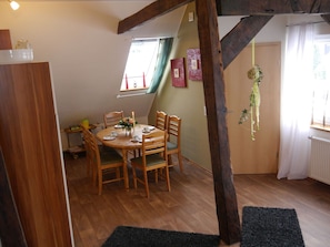 A dining area with a wooden table and chairs, a window with curtains, and a hanging plant. - Ferienwohnung mit Sauna in Lothe (Schieder-Schwalenberg)