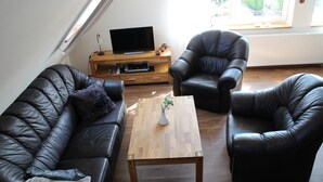 A living room with a sofa, two armchairs, a coffee table, and a TV on a wooden stand.