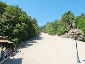 A sandy beach with trees on both sides, a lamp post with flowers, and a few people. - Modern Holiday Home With a South-west Facing Garden (Bergen)