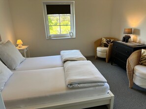 A bedroom with a double bed, a nightstand with a lamp, a chair, a dresser, and a window with a view of greenery. - Apartment, Oldenburg in Holstein (Oldenburg in Holstein)