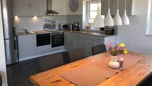 A modern kitchen with grey cabinets, a stainless steel refrigerator, a microwave, a coffee maker, and a clock on the wall. - Apartment, Oldenburg in Holstein (Oldenburg in Holstein)