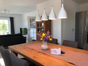 A modern kitchen with a wooden dining table, a vase with flowers, and a refrigerator. - Apartment, Oldenburg in Holstein (Oldenburg in Holstein)