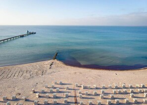 A beach with rows of white tents arranged in a grid pattern, a pier extending into the water, and a clear sky. - Apartment, Oldenburg in Holstein (Oldenburg in Holstein)