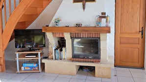 A living room with a fireplace, wooden staircase, and a television on a stand. - Holiday Home in Vosges With Garden and BBQ (Haut-du-Them-Château-Lambert)