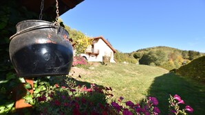 A hanging black pot, a house with a red roof, and a grassy hill with flowers. - Holiday Home in Vosges With Garden and BBQ (Haut-du-Them-Château-Lambert)