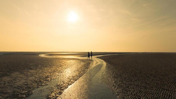 A beach scene with a curved path leading to the water, a person walking, and the sun low on the horizon. - Holiday Home Zoutkamp Near Lauwersmeer (Zoutkamp)