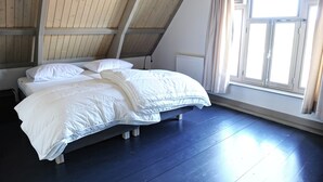 A bedroom with a sloped ceiling, a bed with white bedding, and a window with curtains. - Holiday Home Zoutkamp Near Lauwersmeer (Zoutkamp)