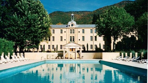 A large building with a swimming pool in front, surrounded by trees and mountains in the background. - Apartment in Rhone Alpes Near Ski Slopes (Montbrun-les-Bains)